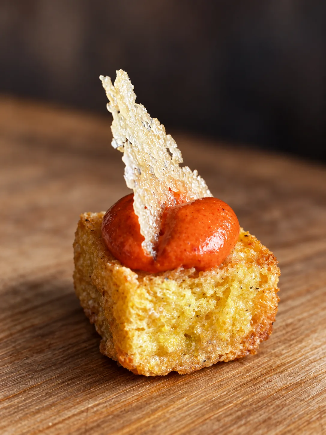 A single crisp bite with a bright sauce and a wafer shard on bare wood