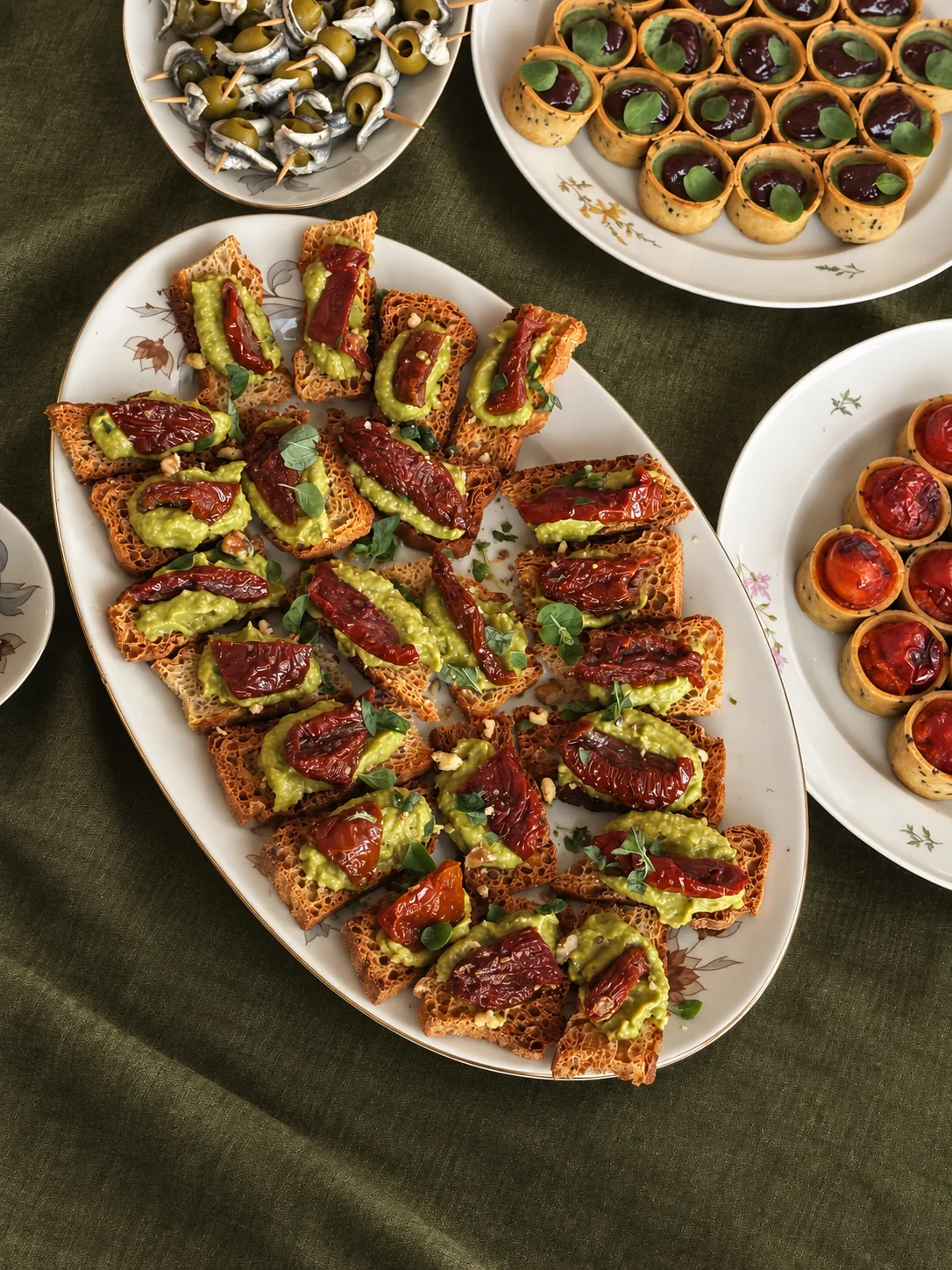 Platters of small bites and tartlets set across a deep green linen cloth
